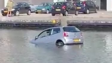 Man op het dak van een auto in het water, terwijl hij lachgas neemt.