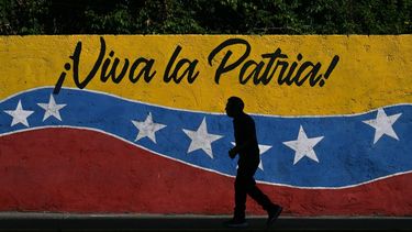 A man walks past a mural depicting the Venezuelan national flag and reading 