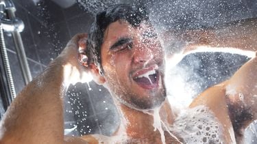 Een foto van een man die onder de douche shampoo uitspoelt