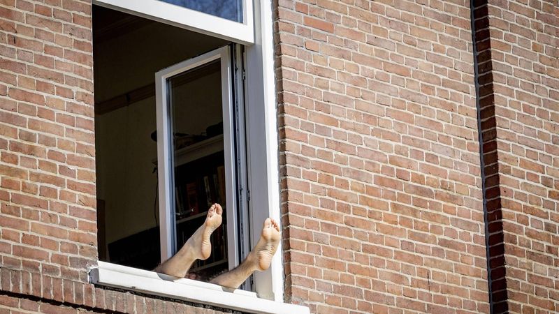 AMSTERDAM - Benen steken uit een raam, op een zonnige dag in de hoofdstad. Het is uitzonderlijk warm voor het jaar. Er is officieel sprake van de warmste 8 maart ooit gemeten. ANP ROBIN UTRECHT