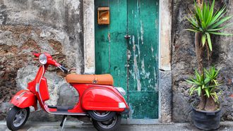 Photo of red scooter near green door and palm