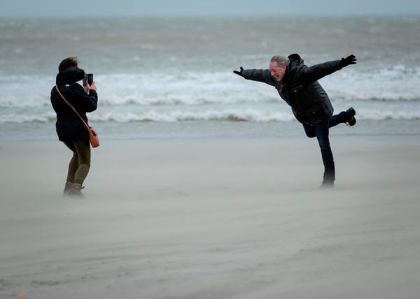 Een man op het strand die op 1 been in de storm hangt