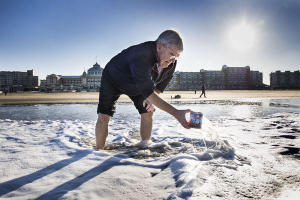 Een foto van burgemeester Van Zanen die water uit de zee schept voor de Nieuwjaarsduik thuis