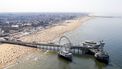 Op deze luchtfoto zie je de pier in Scheveningen en badgasten op het strand. De zomervakantie is in volle gang en door het warme weer liggen de stranden vol.