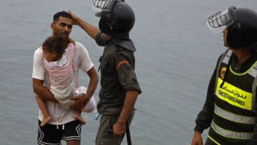 A member of Moroccan security forces gestures to a man carrying a child close to the site of clashes near Fnideq, on the Morocco-Spain border, on July 31, 2026. Thousands of migrants crossed overnight from Morocco into Spain's north Africa's Ceuta enclave, a police source said on July 31, as Prime Minister Pedro Sanchez was set to arrive to manage the latest migrant crisis on the border.
Abdel Majid BZIOUAT / AFP