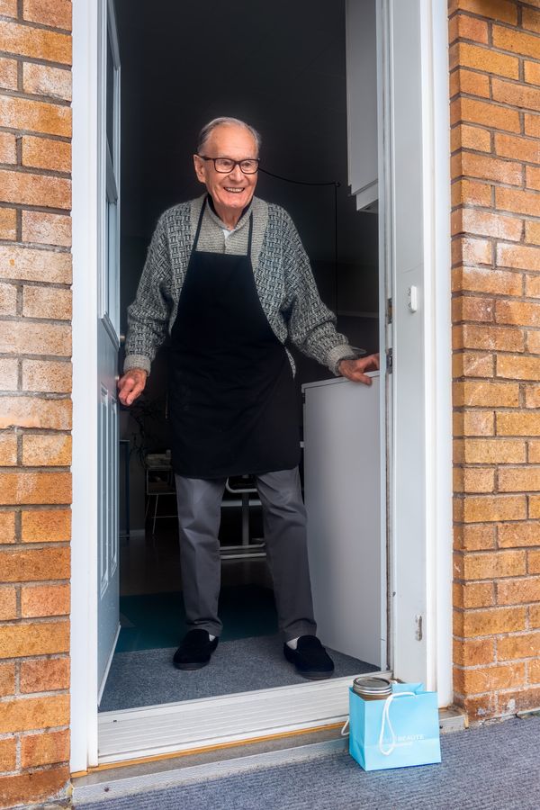Een foto van een oudere man in de deur bij wie een tasje boodschappen op de stoep is gezet.