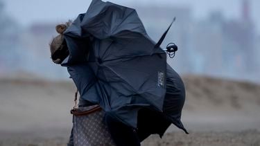 Een foto van een vrouw op het strand met een kapot gewaaide paraplu in de storm