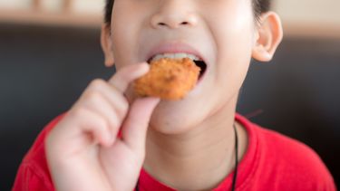 Een foto van een kipnugget in de mond van een jongetje