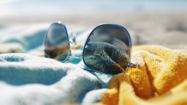 Op deze foto zie je een zonnebril op een stapeltje handdoeken liggen op het strand