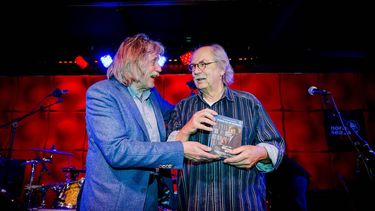 AMSTERDAM - Johan Derksen (L) overhandigt het eerste exemplaar van Derksen On The Road aan gitarist Jan de Hont. Het boek bevat 2 cd's met muziek van zijn helden en een dvd met acht afleveringen van de gelijknamige tv-serie. ANP  ROBIN VAN LONKHUIJSEN