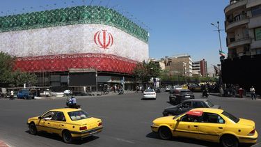 Traffic moves past the Iranian national flag displayed on a building at Enghelab square in Tehran on June 14, 2026. US President Donald Trump said that a deal with Iran to end the Middle East war could be signed on June 14, and that the strategic Strait of Hormuz would be 