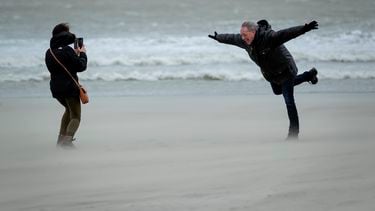 Een man op het strand die op 1 been in de storm hangt