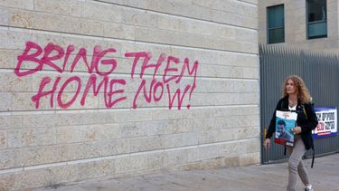 2023-11-18 16:10:20 A woman holding an image of 26-year-old Israeli hostage Ziv Berman walks past graffiti calling for the release of Israeli hostages held in the Gaza Strip since the October 7 attack by Hamas militants in southern Israel, in Jerusalem on November 18, 2023, amid the ongoing battles between Israel and the Palestinian group Hamas. 
GIL COHEN-MAGEN / AFP