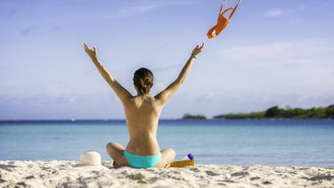 Een foto van een topless dame op het strand, op de rug gezien