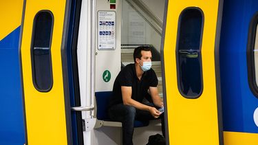 Op deze foto zie je een man in trein met een mondkapje