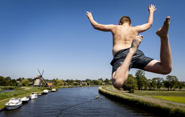 Een foto van een jongetje dat vanaf een brug in het water springt