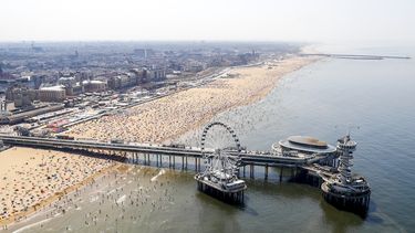 Op deze luchtfoto zie je de pier in Scheveningen en badgasten op het strand. De zomervakantie is in volle gang en door het warme weer liggen de stranden vol.