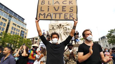 Een foto van demonstranten voor het monument op de Dam, een man houdt een bord met de tekst black lives matter omhoog. Korpschef: Er zijn fouten gemaakt bij inschatting.