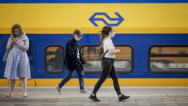 Op deze foto zijn treinreizigers te zien, met een mondkapje op. Ze lopen langs een NS-trein op het perron.