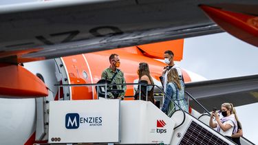 Een foto van passagiers met een mondkapje die een vliegtuig binnenstappen
