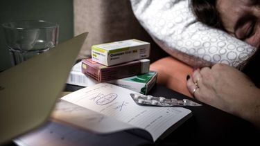 توضيحية - امرأة في السرير مع جهاز كمبيوتر محمول مغلق، وجدول أعمال يحتوي على أيام عمل محذوفة وأدوية مضادة للاكتئاب على الطاولة بجانب السرير. آنب روب إنجيلار